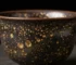Authentic Jian Zhan tea cup showing natural oil spot glaze pattern with golden crystalline droplets on dark ceramic surface, demonstrating real Tenmoku kiln transformation