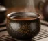 Handmade Jian Zhan tea cup with oil spot glaze pattern, filled with steaming hot amber tea showing excellent heat retention on a wooden tea tray