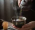 A Jian Zhan Tenmoku tea cup with deep amber tea being poured in, showing oil spot metallic glaze pattern
