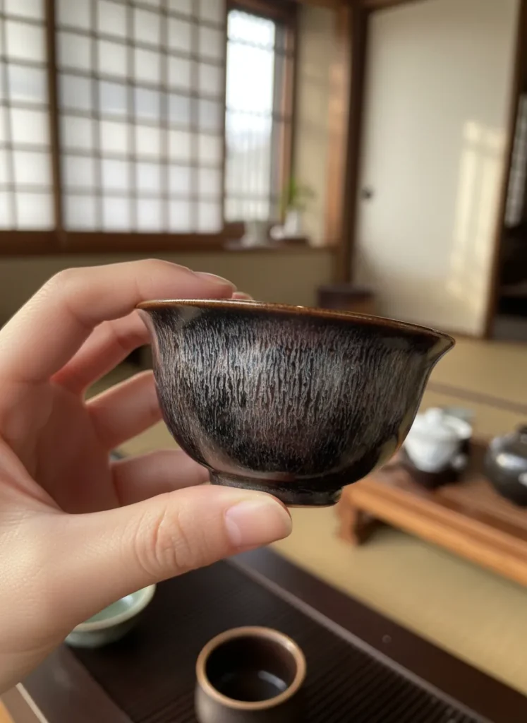 How to Season Your Jian Zhan Cup for Better Tea Flavor 5 Hand holding a Jian Zhan tea cup with hare's fur glaze pattern, inspecting the subtle lustrous sheen of the seasoned patina
