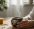Hands holding a dark Tenmoku tea cup with oil spot glaze during a peaceful morning mindfulness ritual, steam rising from golden oolong tea