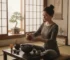 Woman performing a gongfu tea ritual with a dark Tenmoku bowl at a low wooden table, pouring tea from a clay teapot in a meditative setting