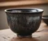 Handmade Jian Zhan tea cup featuring hare's fur glaze pattern with fine silver streaks radiating from rim to base on dark black ceramic