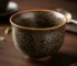 Elegant tenmoku tea cup with oil spot glaze pattern golden metallic droplets on dark ceramic catching light